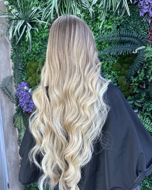 Lange blonde Wellen vor der Pflanzenwand im Show Coiffeur Hagen